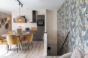 Une cuisine moderne dotée d’un four encastré, d’un coin repas avec des chaises jaunes et d’un papier peint à motifs.