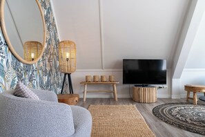 Een moderne woonkamer met een grijze bank, een grote flatscreen-tv, een houten salontafel, rieten lampen en een kamerkleed met een patroon.