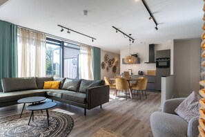 Un salon moderne avec un canapé d’angle, une petite table basse et un coin repas avec des chaises.