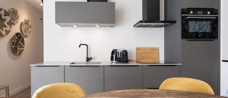 A modern kitchen with grey cabinetry, a stainless steel range hood, and a built-in oven.