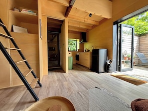A compact living space with a wooden interior, a built-in kitchen, and a sliding glass door leading to an outdoor area. - Tiny house with fireplace in polder | Tiny House Wood (Groede)