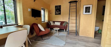 Una habitación acogedora con techo de madera, un sofá, una silla, una mesita y una escalera.