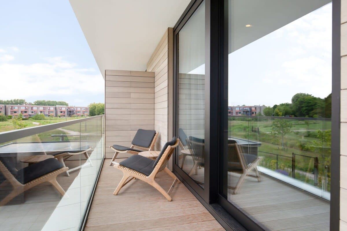Un balcón con sillas de mimbre y una mesa de vidrio, con vista a una zona residencial.