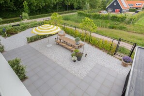 An outdoor patio area with a wooden table and chairs, a striped umbrella, and potted plants. - Studio with AC in Domburg | Summum Suites 3 (Domburg)