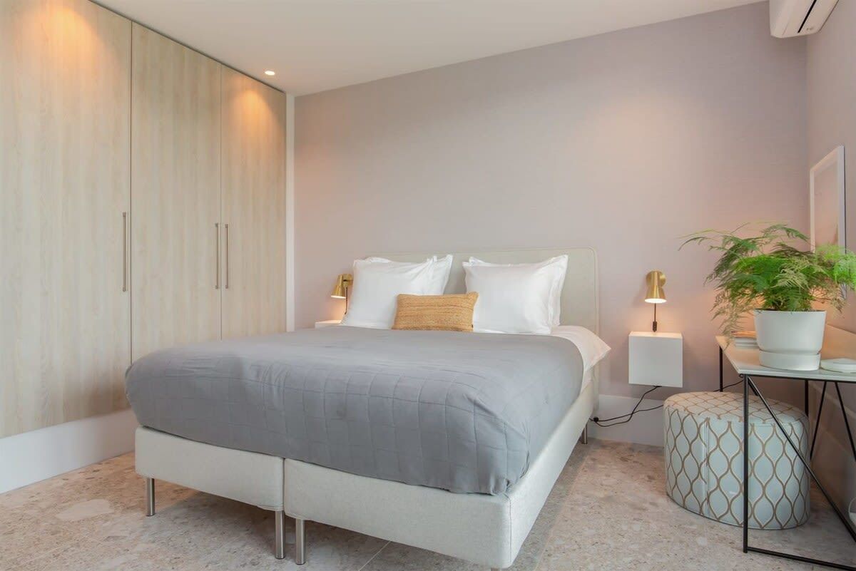 Un dormitorio moderno con una cama grande, lámparas de noche, un armario y una mesita con una planta.