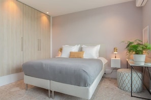 Une chambre à coucher moderne avec un lit, des lampes de chevet, une armoire et une plante en pot.