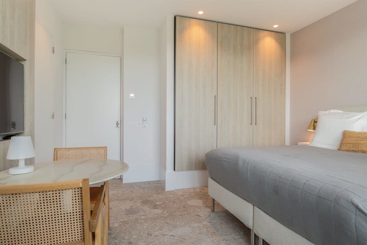 Un dormitorio con cama, mesita de noche con lámpara, armario y televisor.