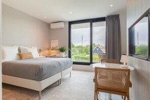 A modern bedroom with a large bed, a dining table, and a view of greenery and a house outside the window. - Studio with AC in Domburg | Summum Suites 3 (Domburg)