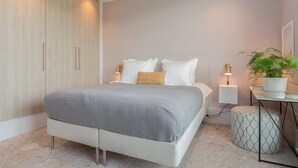 A modern bedroom with a large bed, bedside lamps, a wardrobe, and a small table with a plant.