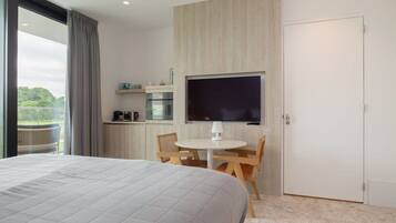 Een moderne hotelkamer met een groot bed, een zithoek met tafel en stoelen, een aan de muur bevestigde televisie en uitzicht op het omliggende landschap.