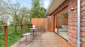 A balcony with a wooden deck, metal chairs, a table, and a glass door leading to an interior space.