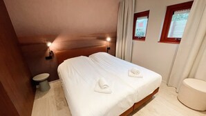 A hotel room with a large bed, two bedside tables, a small toilet, and a window with curtains. - Apartment in the centre of Domburg | Duinenburg 10-3 (Domburg)