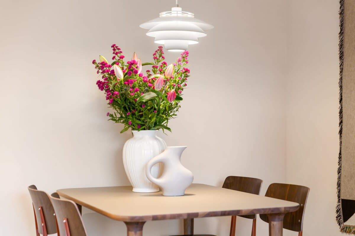 Ein Essbereich mit Tisch, Stühlen, einer Vase mit Blumen und einer Pendelleuchte.