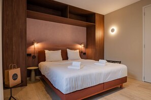 Ein modernes Hotelzimmer mit einem großen Bett, einem Holzkopfteil, Nachttischlampen und einer runden Wandleuchte.