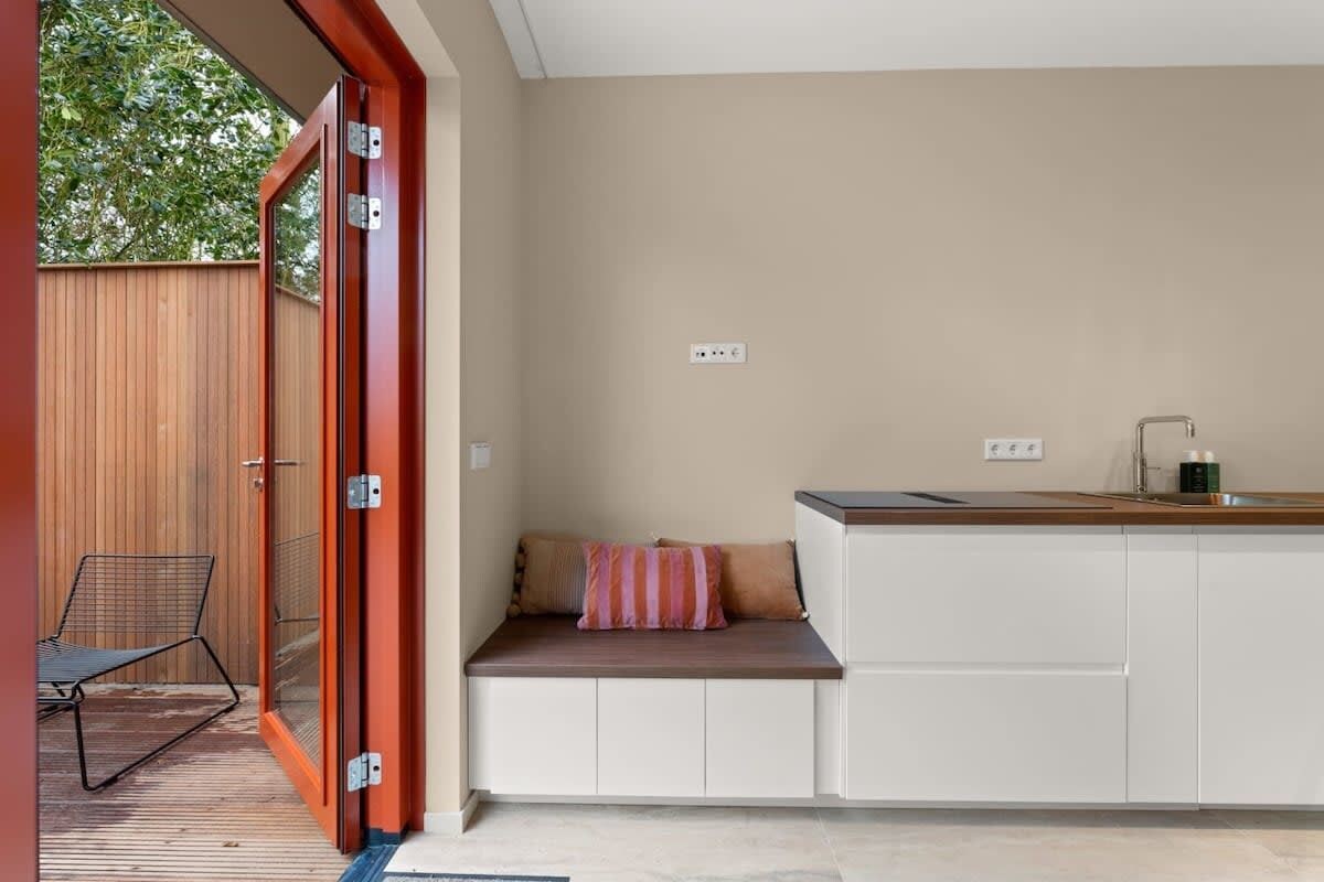 Eine moderne Küche mit integriertem Sitzplatz, einer Holztür und Blick ins Freie.