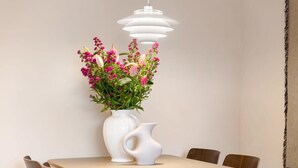A dining area with a table, chairs, a vase with flowers, and a pendant light. - Apartment in the centre of Domburg | Duinenburg 10-3 (Domburg)