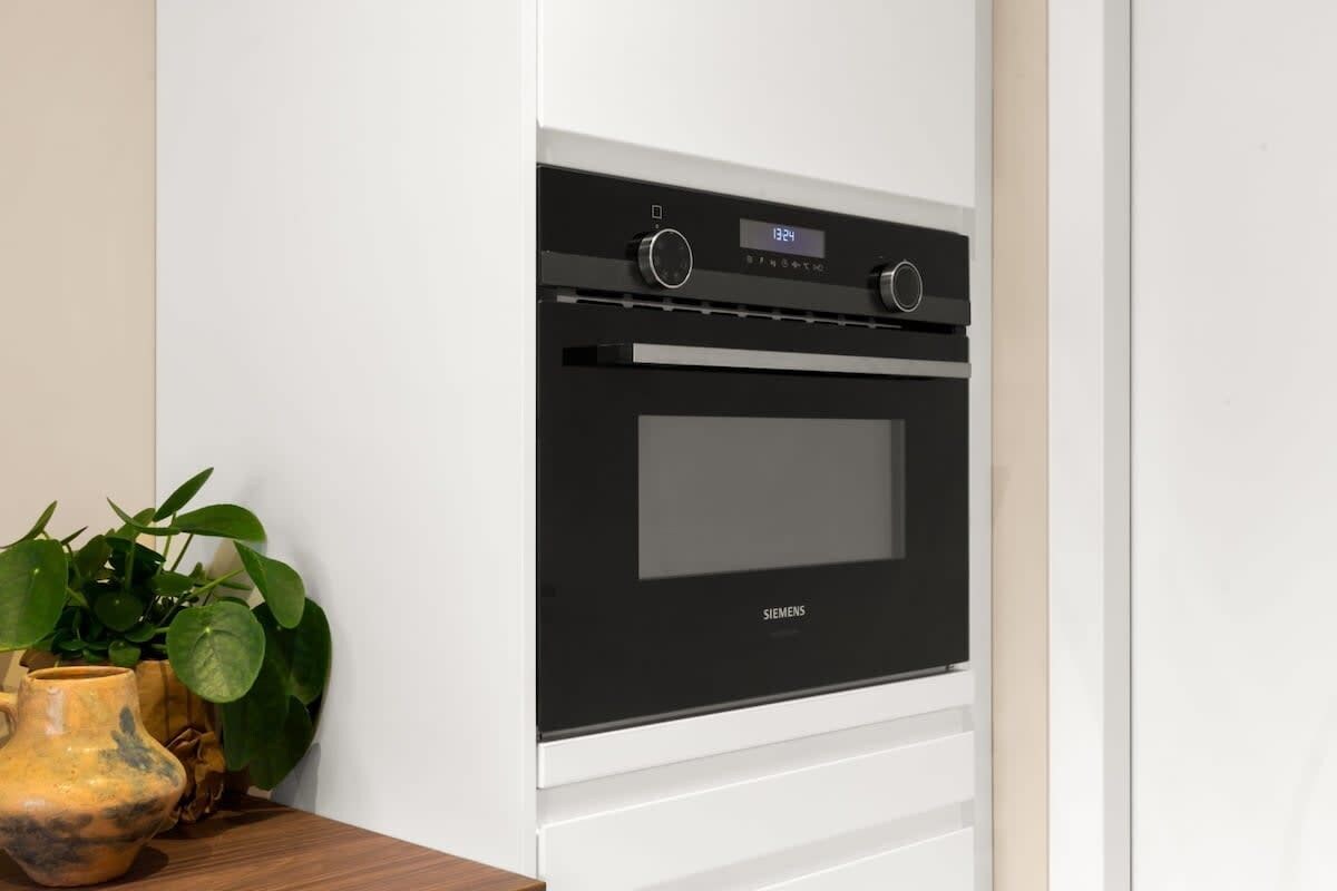 Een moderne keuken met een zwarte oven, witte kasten en een plant op het aanrecht.