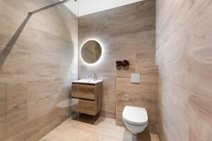 Une salle de bain moderne avec une douche à parois de verre, un meuble-lavabo en bois, un miroir rond et des toilettes.