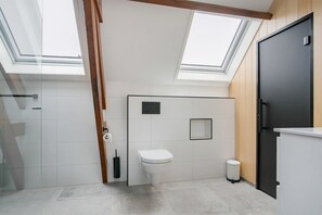 A modern bathroom with skylights, a toilet, a trash bin, and a black cabinet.