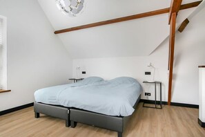 A bedroom with a bed, bedside tables, a ceiling light fixture, and wooden beams.