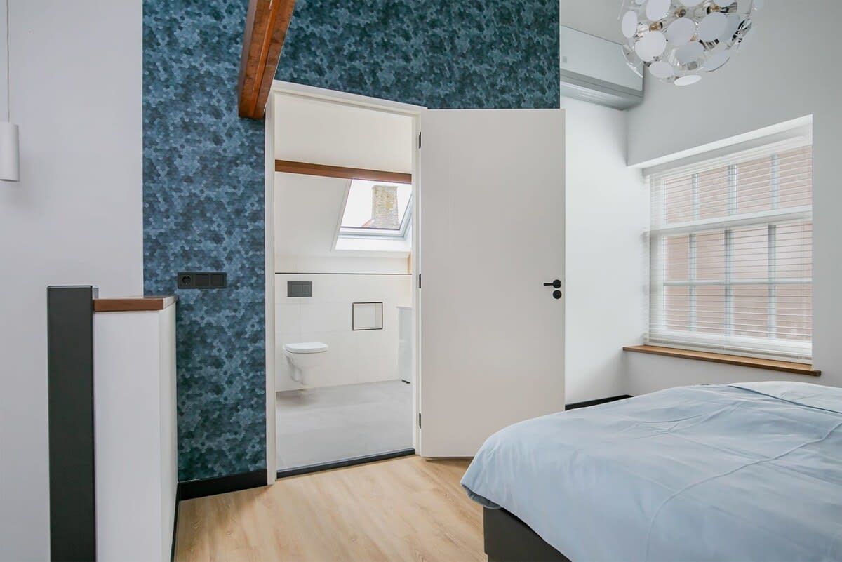Une chambre à coucher comprenant un lit, une armoire, un puits de lumière et une fenêtre avec des stores.