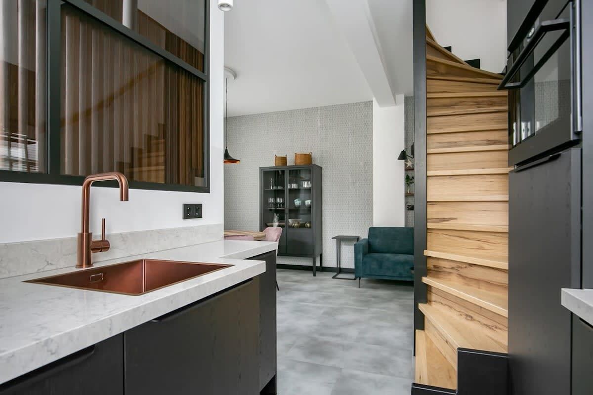 Une cuisine moderne avec un évier en cuivre, des meubles de couleur sombre et un mur d’accent en bois.