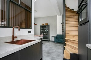 Una cocina moderna con un lavamanos de cobre, muebles oscuros y una pared decorativa de madera.