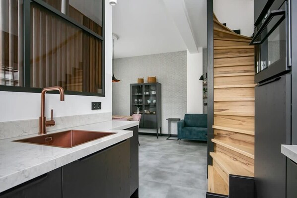 A modern kitchen with a copper sink, dark cabinetry, and a wooden accent wall.