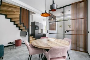 Una cocina moderna con una escalera de madera, una zona de comedor con sillas rosadas y un ventanal grande.