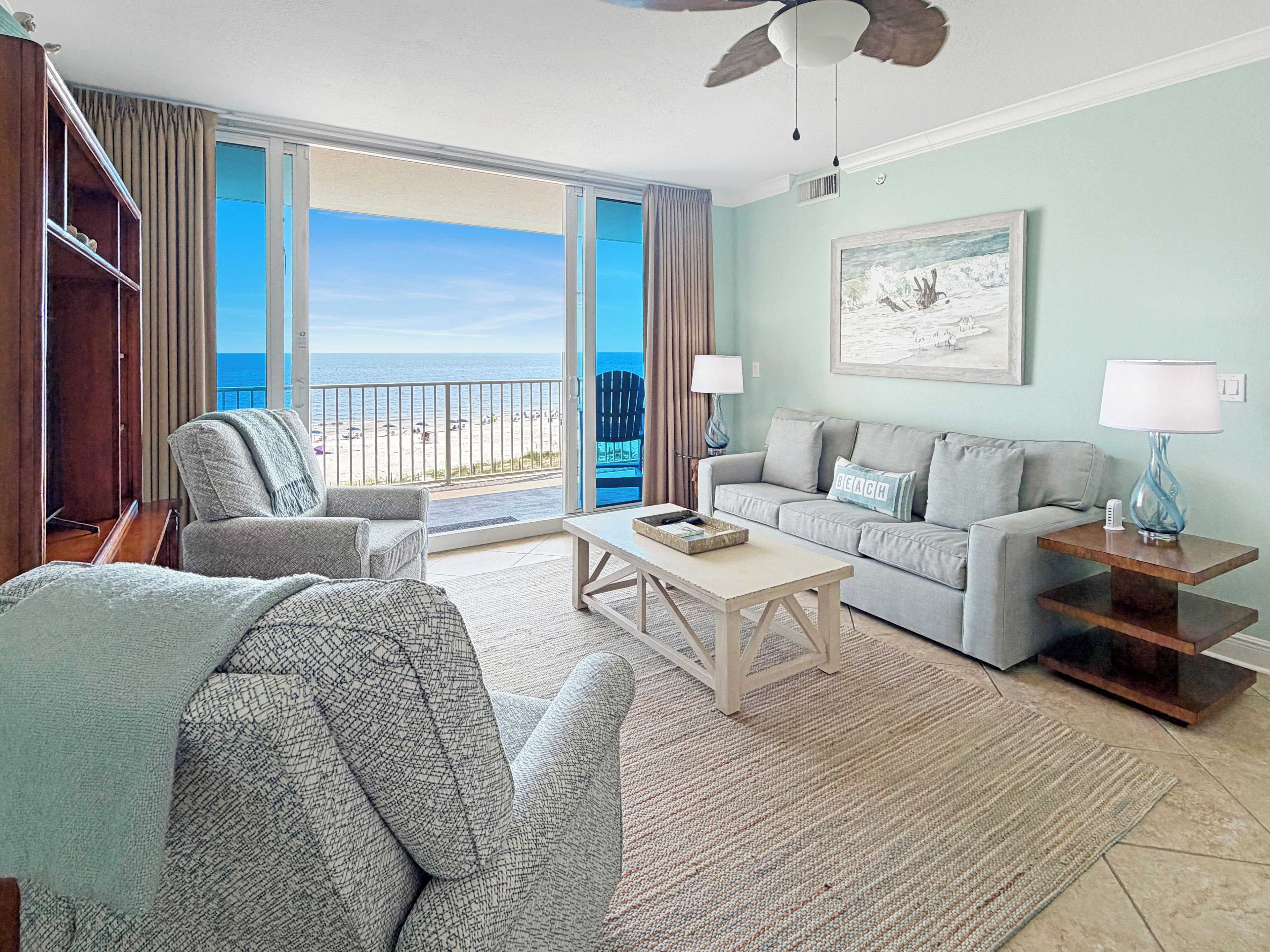 A living room with a balcony overlooking the beach, a sofa, a coffee table, and a lamp.