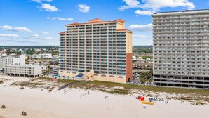 A high-rise hotel with multiple balconies, a beach in the foreground, and a clear blue sky. - Luxury Beachfront condo - 3 Bedroom, 3 full Bath, 2 master suites, sleeps 8. (Gulf Shores)