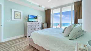 A bedroom with a large bed, a dresser, a television, and a view of the ocean. - Luxury Beachfront condo - 3 Bedroom, 3 full Bath, 2 master suites, sleeps 8. (Gulf Shores)