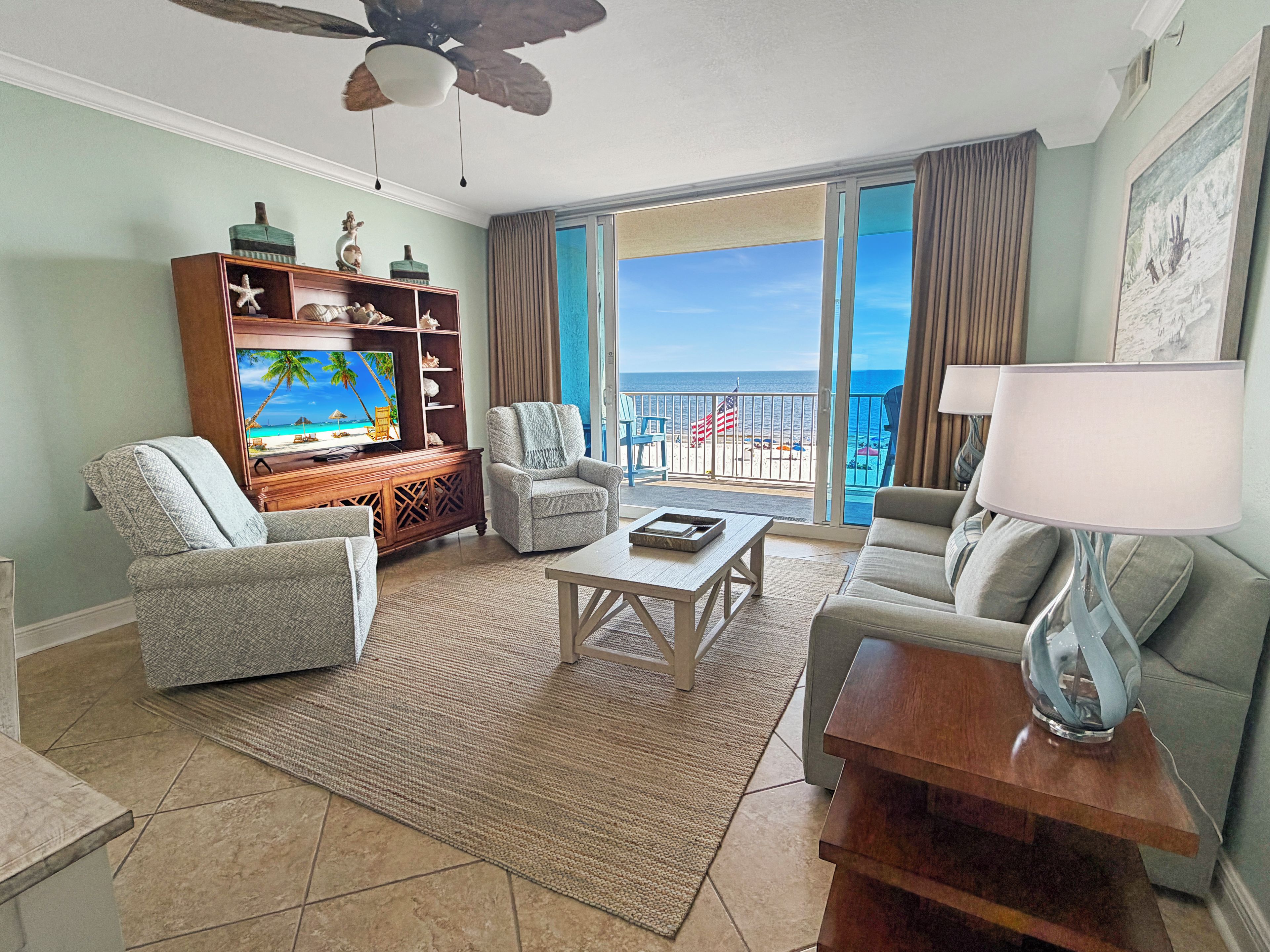 A living room with a television, seating, a coffee table, and a view of the ocean through large windows.