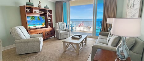 A living room with a television, seating, a coffee table, and a view of the ocean through large windows.