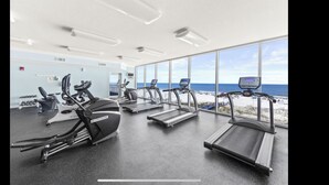 A gym with treadmills and elliptical machines, large windows with a beach view, and a clean, modern design. - Luxury Beachfront condo - 3 Bedroom, 3 full Bath, 2 master suites, sleeps 8. (Gulf Shores)