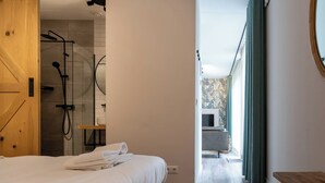 A hotel room with a bed, a wooden door, a shower area, and a view of the outside. - Apartment near the beach in Oostkapelle | Duno Lodge 15-G (Oostkapelle)