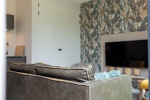 Un salon moderne avec un canapé, un téléviseur à écran plat et un mur orné d’un motif.
