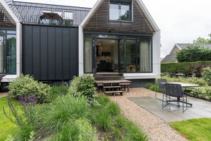 Ein modernes Haus mit einer großen Glasdoor, die zu einer Küche führt, umgeben von einem gepflegten Garten und einer Sitzgelegenheit im Freien.