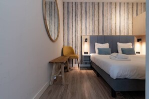 Une chambre d’hôtel avec un lit, une table de chevet, une chaise et un grand miroir.