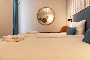 Une chambre d’hôtel avec un lit, un miroir rond orné de motifs floraux, une table de chevet et un oreiller bleu.