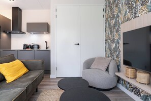 Un espace de vie moderne comprenant un canapé, un fauteuil et un téléviseur à écran plat posé sur une étagère en bois.