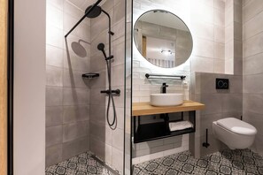 Une salle de bain moderne avec une douche à parois de verre, un miroir rond, un lavabo blanc et des toilettes.