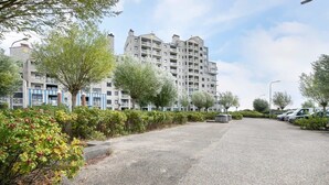 En bygning med flere etager, altaner, en parkeringsplads og en række parkerede biler.