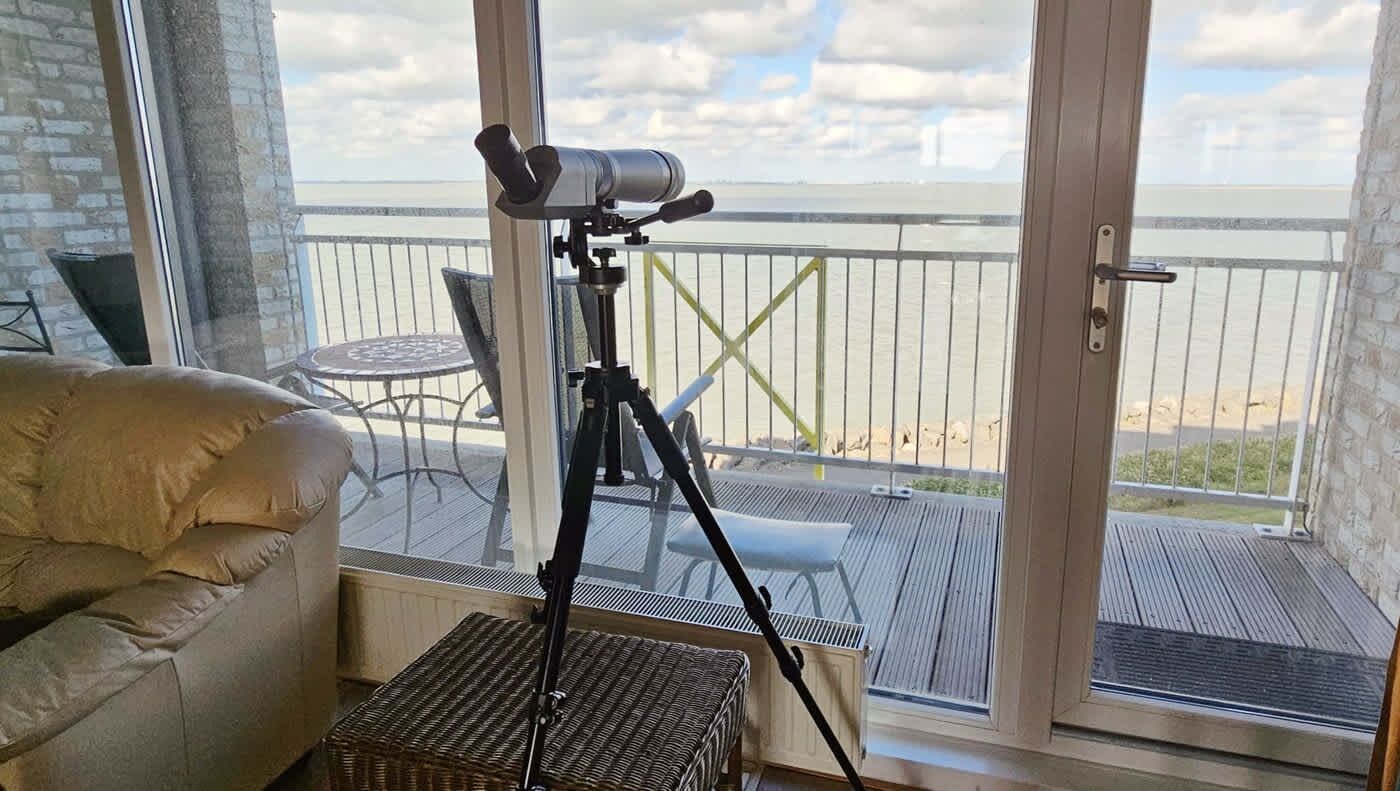 En balkong med ett teleskop, möbler i rotting och utsikt över havet.