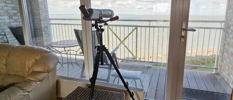 Un balcón con un telescopio, muebles de mimbre y vistas al mar.