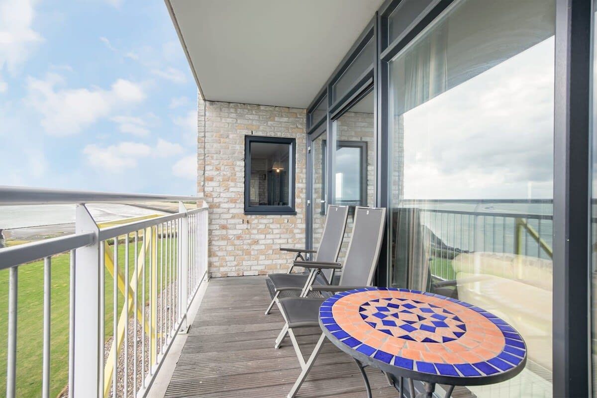 A balcony with a view of the sky, a tiled table, and two chairs.