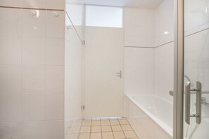 A modern bathroom with white tiles, a glass shower enclosure, and a white bathtub.