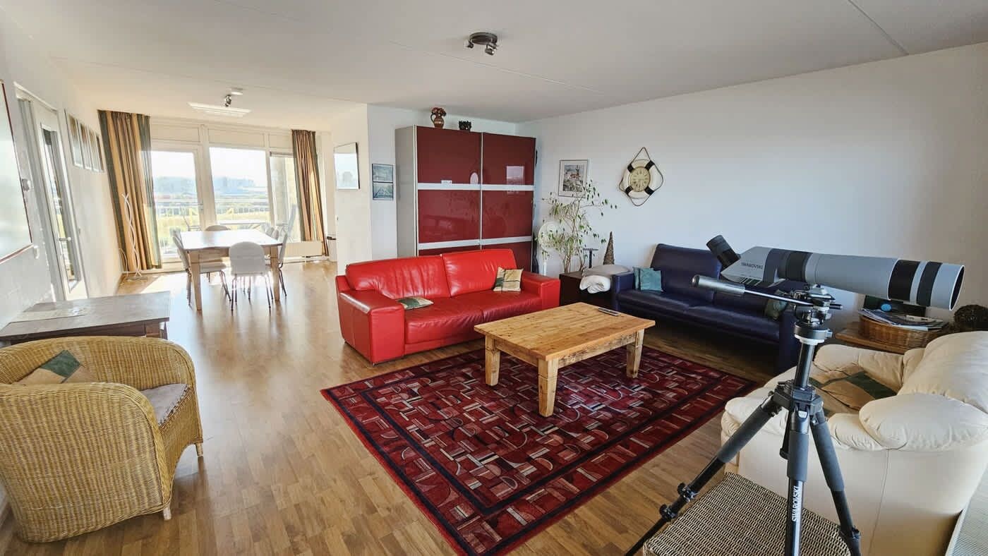 A living room with a red sofa, a wooden coffee table, a blue sofa, and a telescope on a tripod.