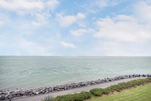 A coastal walkway with a stone barrier, grassy areas, and a view of the sea.