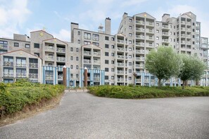 A multi-story residential building with balconies, a gated entrance, and a landscaped area with trees.